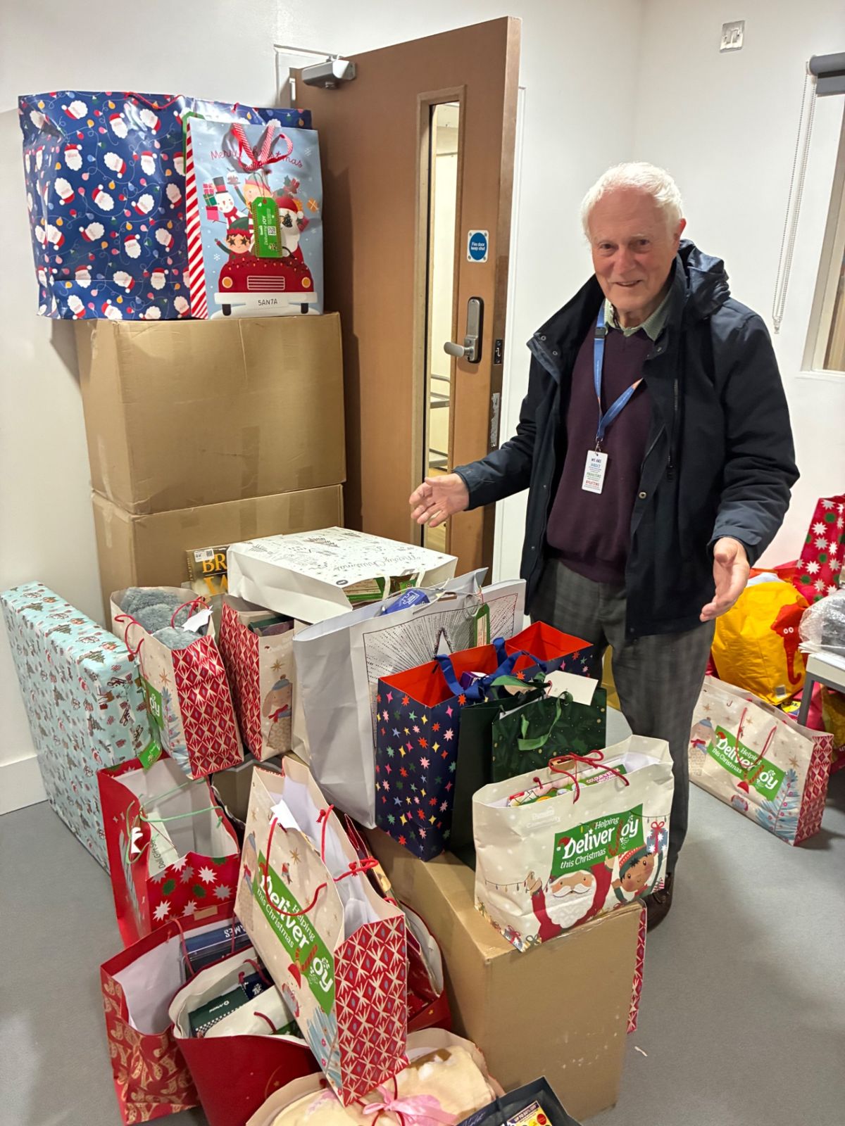 A smiling volunteer standing among wrapped gifts prepared for families